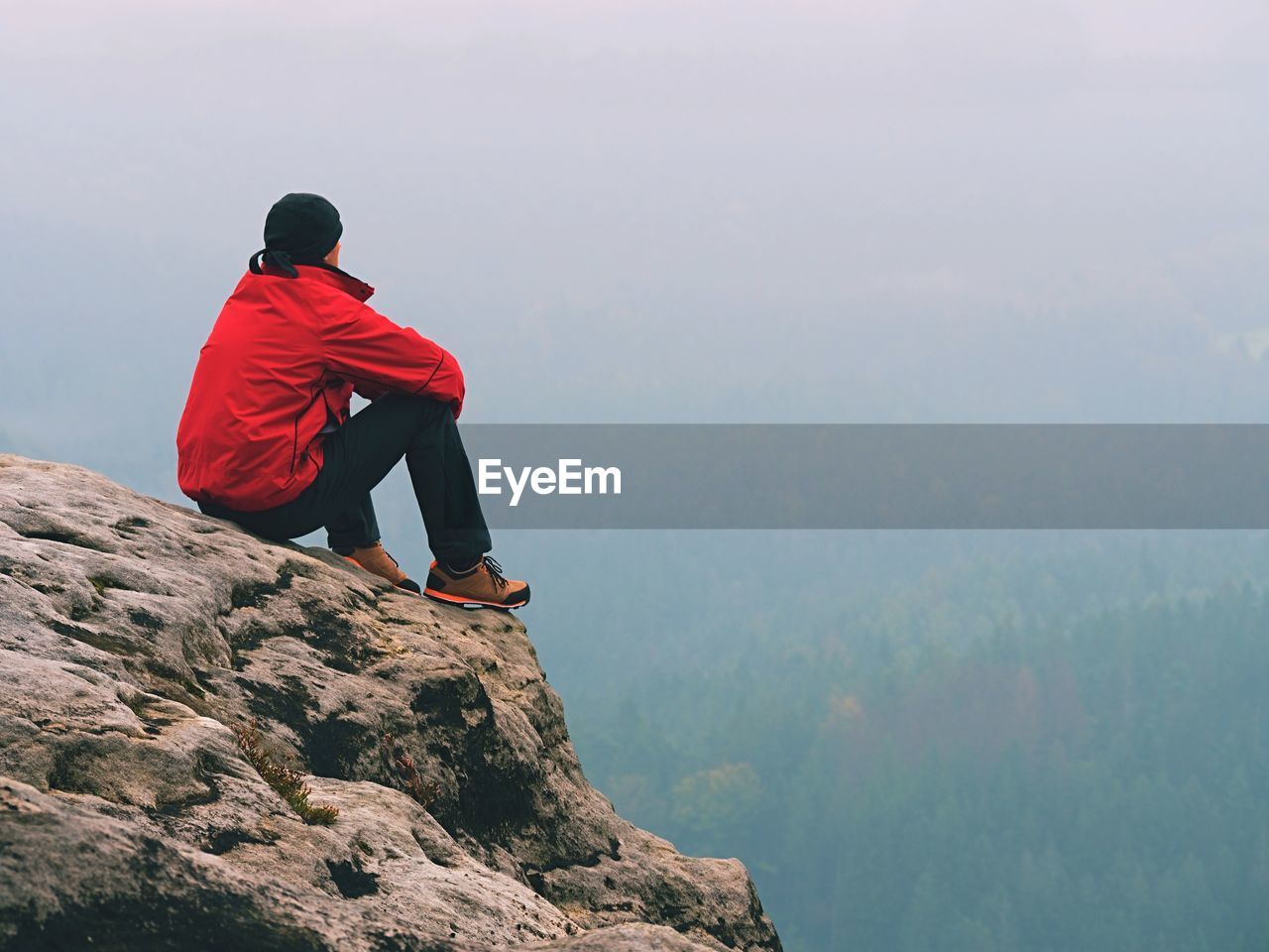 Hiker man take a rest on mountain peak. man sit on sharp summit and enjoy spectacular view.