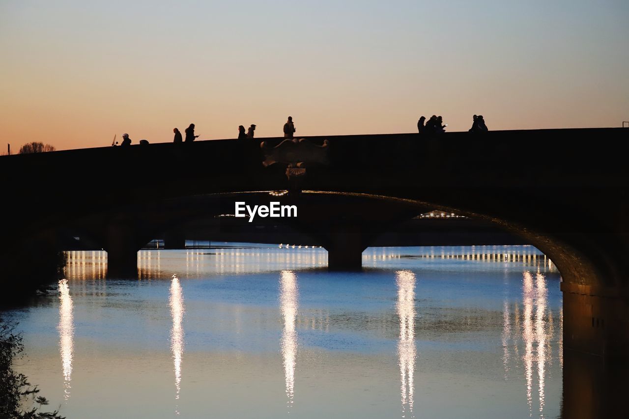 BRIDGE OVER RIVER AGAINST CLEAR SKY DURING SUNSET