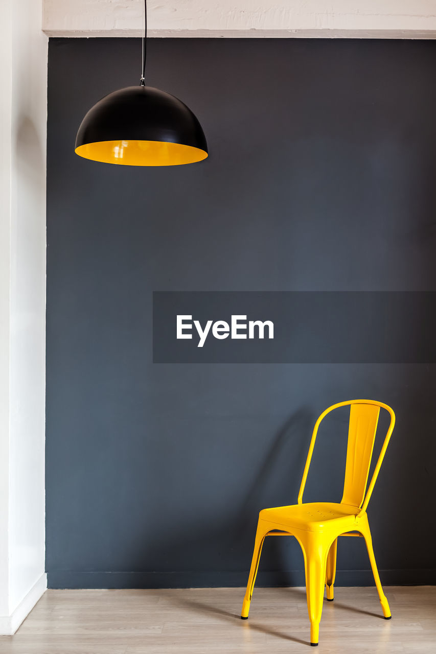 EMPTY CHAIR AND TABLE AGAINST YELLOW WALL