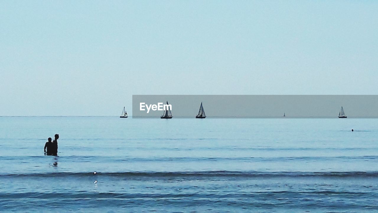 SILHOUETTE MAN STANDING IN SEA AGAINST CLEAR SKY