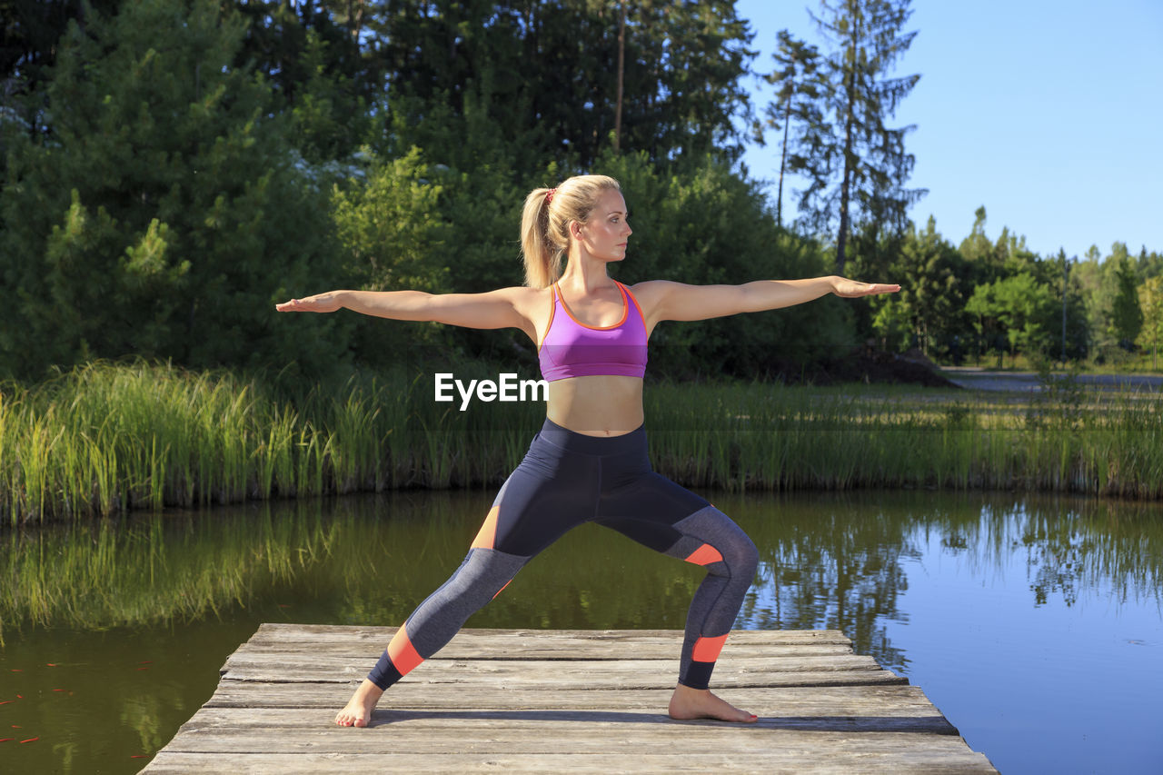 Woman exercising on pier over lake against trees