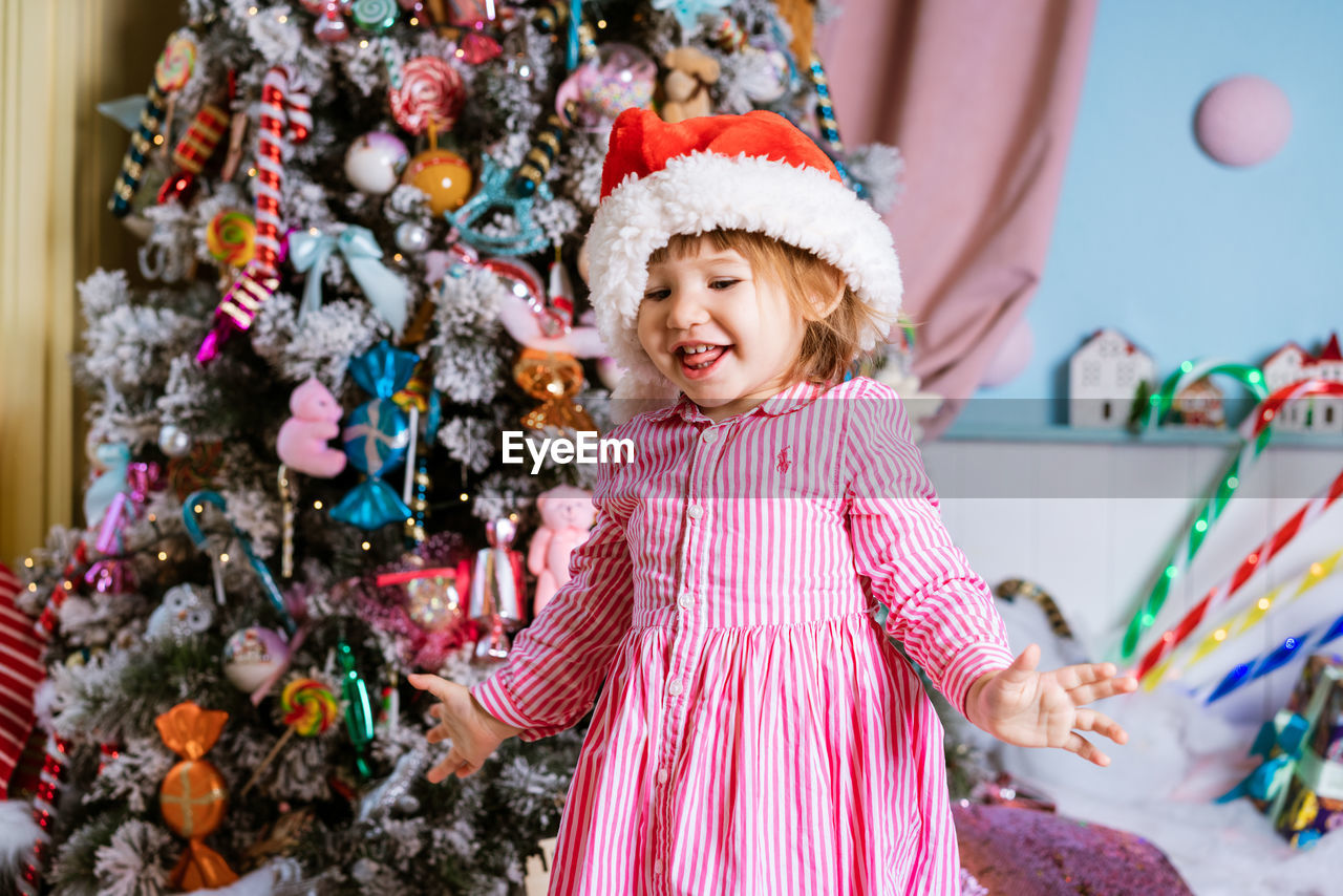 Funny child little girl in santa claus hat and pink dress laughs with happiness