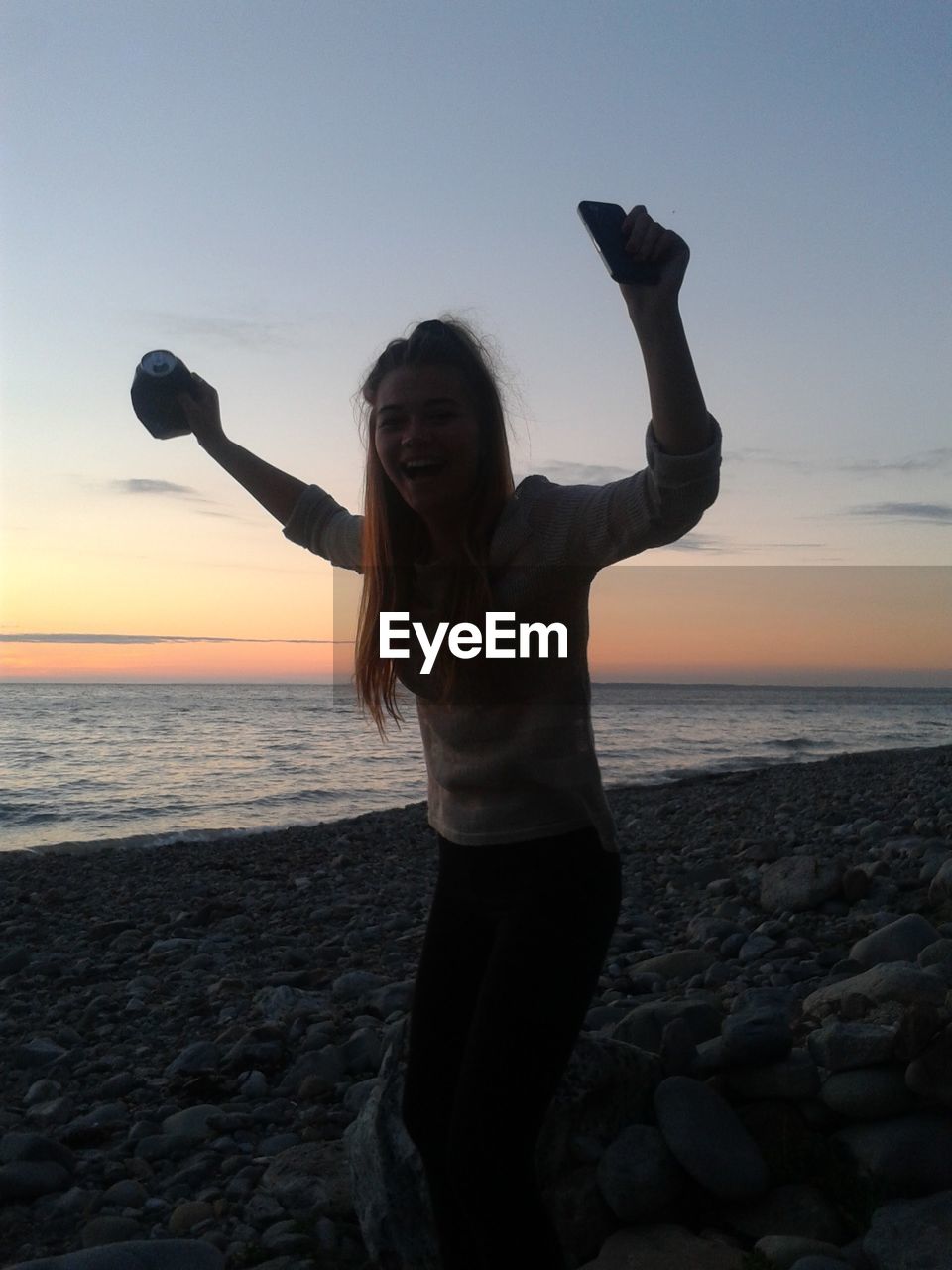 Portrait of excited woman shouting while standing at beach during sunset