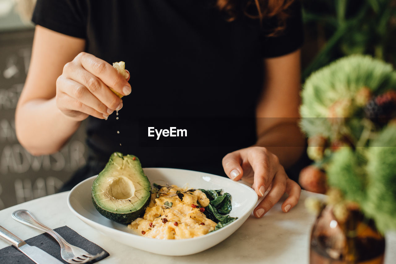 Midsection of woman eating scrambled eggs and avocado for breakfast