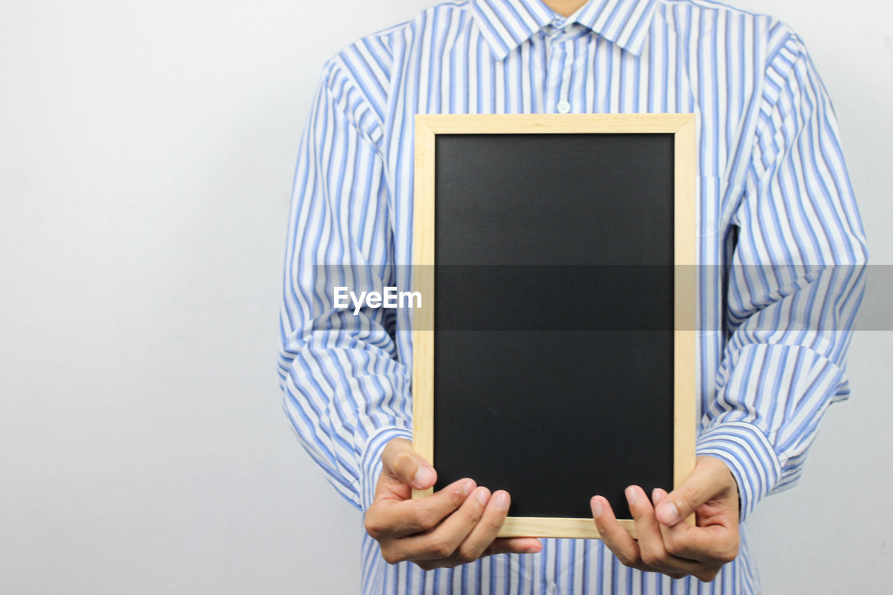 Close-up of man holding blank blackboard against white background