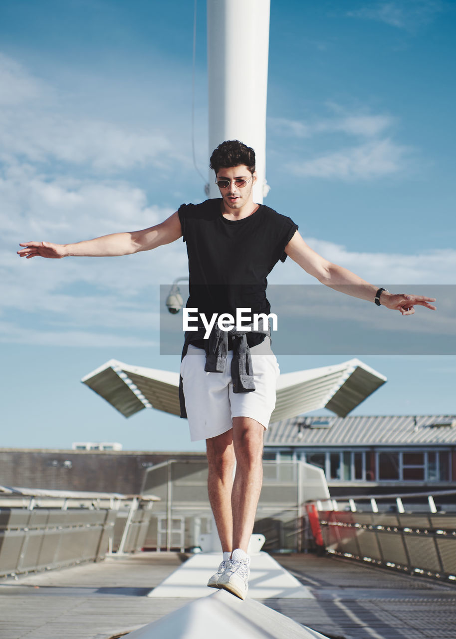 Young man with arms outstretched standing against sky