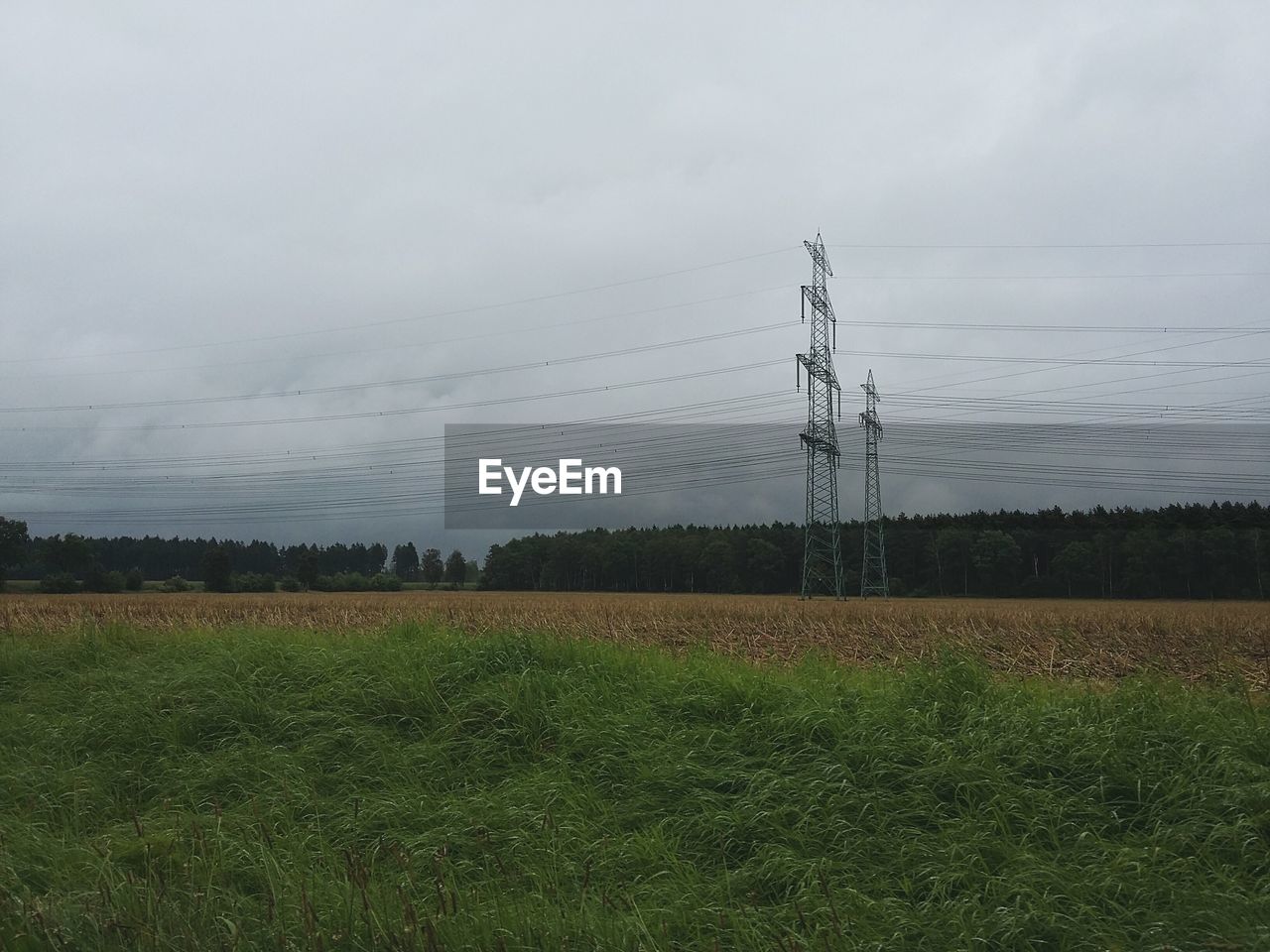 ELECTRICITY PYLON ON GRASSY FIELD AGAINST CLOUDY SKY