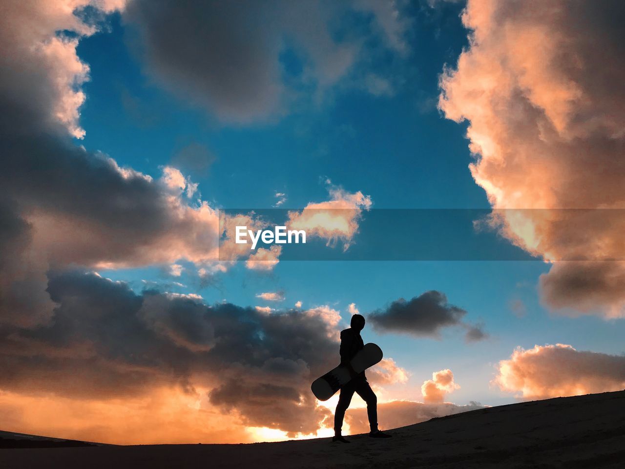 Silhouette man standing on sand dune against sky during sunset