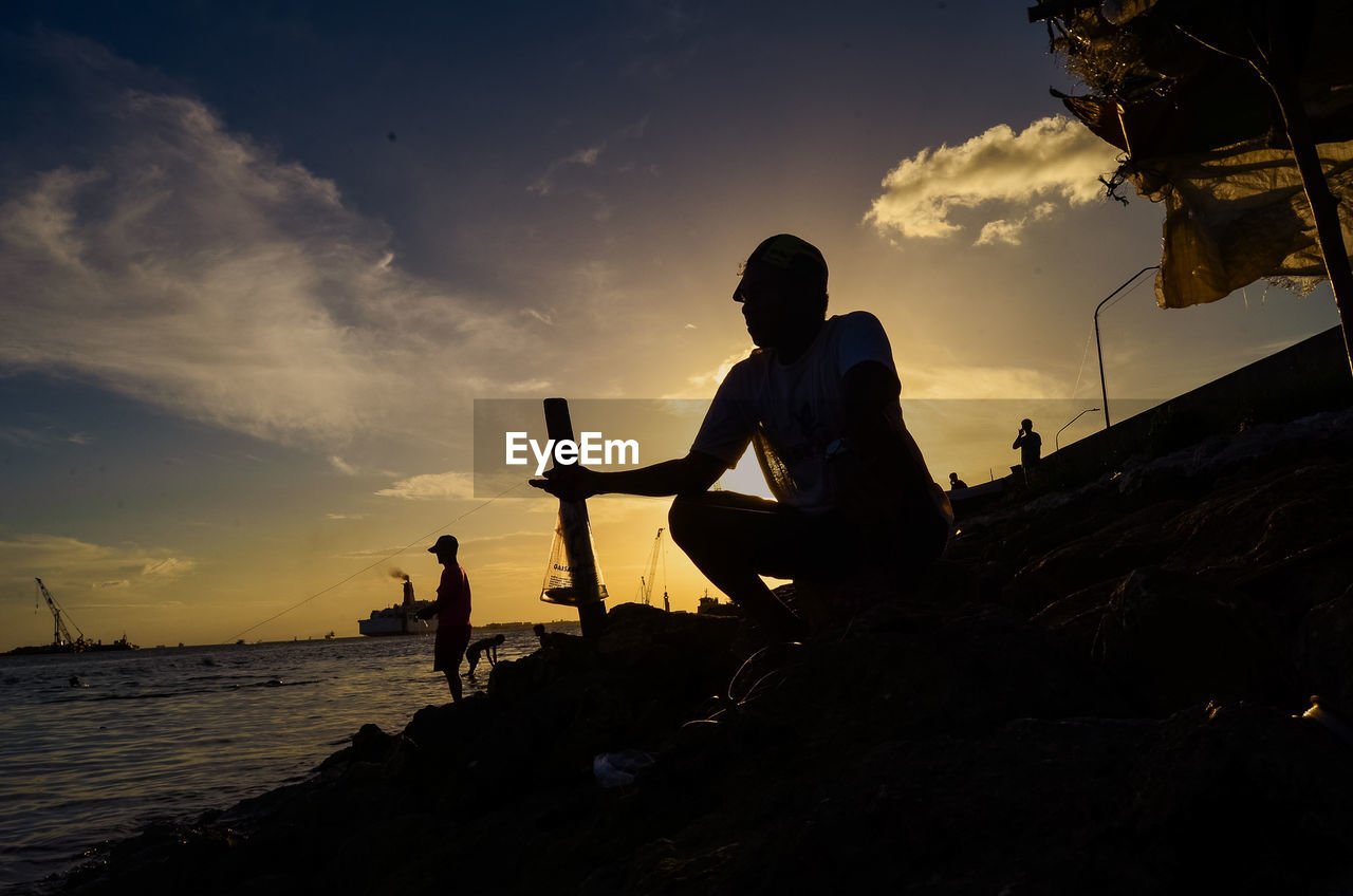 SILHOUETTE PEOPLE STANDING BY SEA AGAINST SKY DURING SUNSET