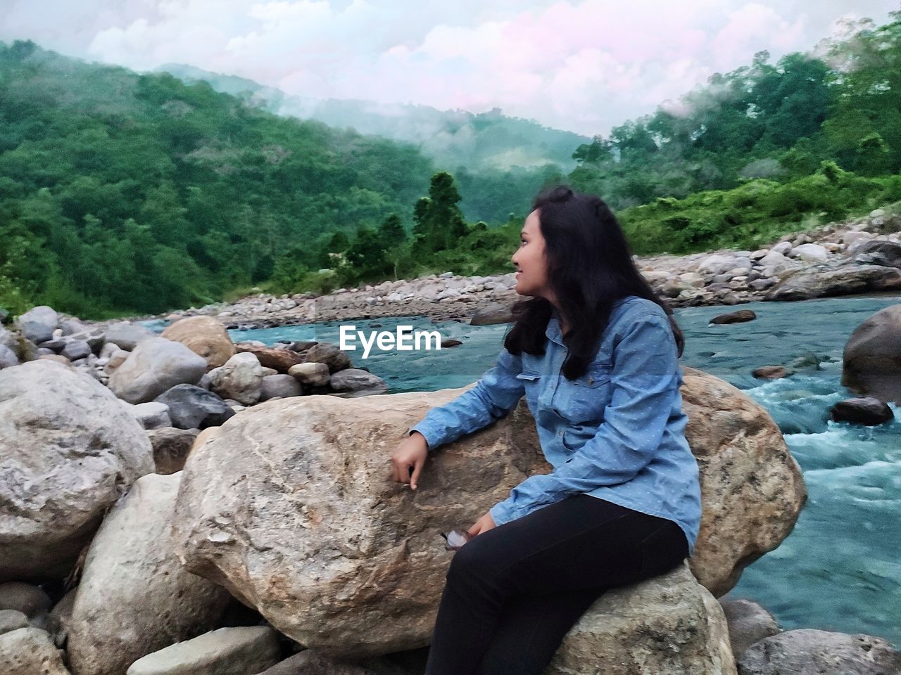 YOUNG WOMAN SITTING ON ROCK BY ROCKS