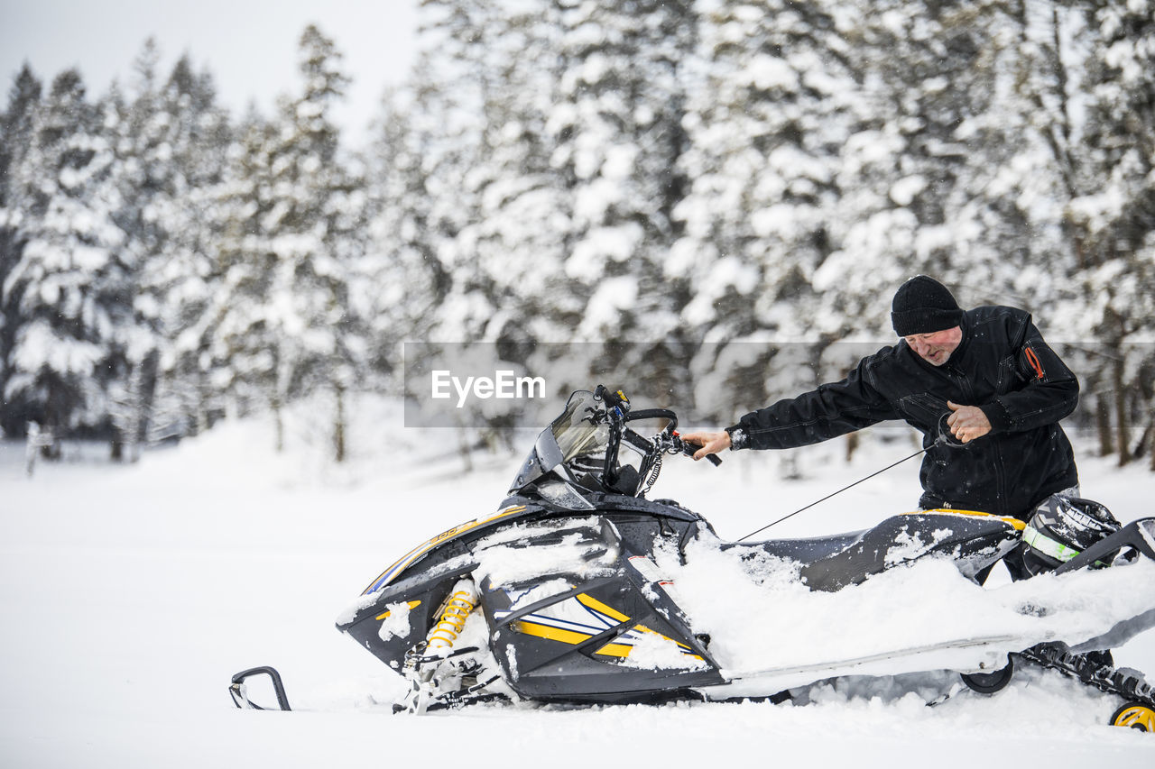 Senior man starting snowmobile with pull cord.