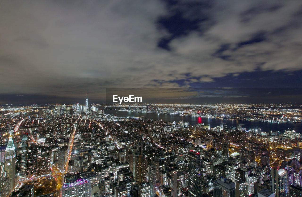 Illuminated cityscape against cloudy sky at night