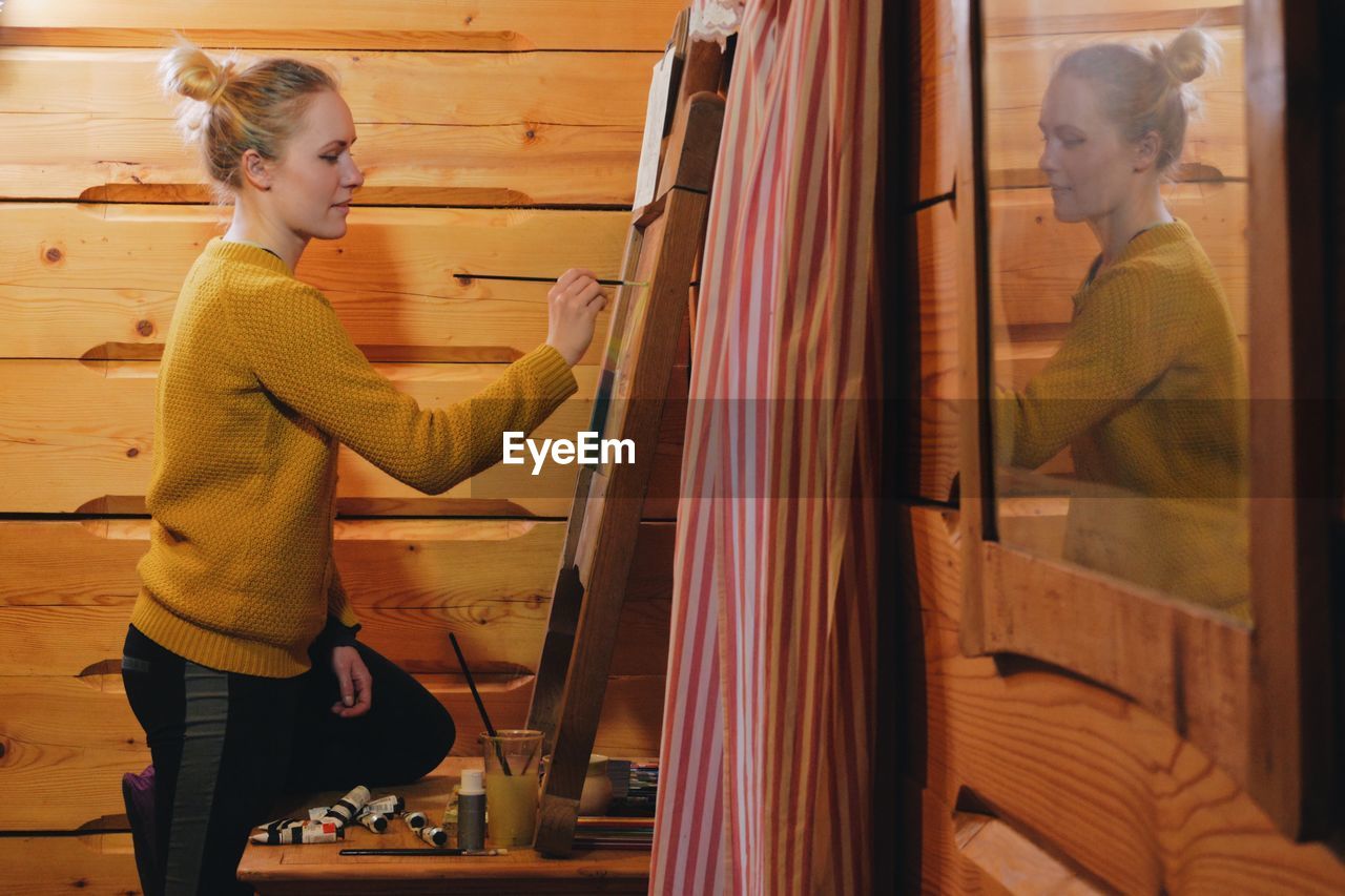 Side view of woman drawing on canvas in cottage