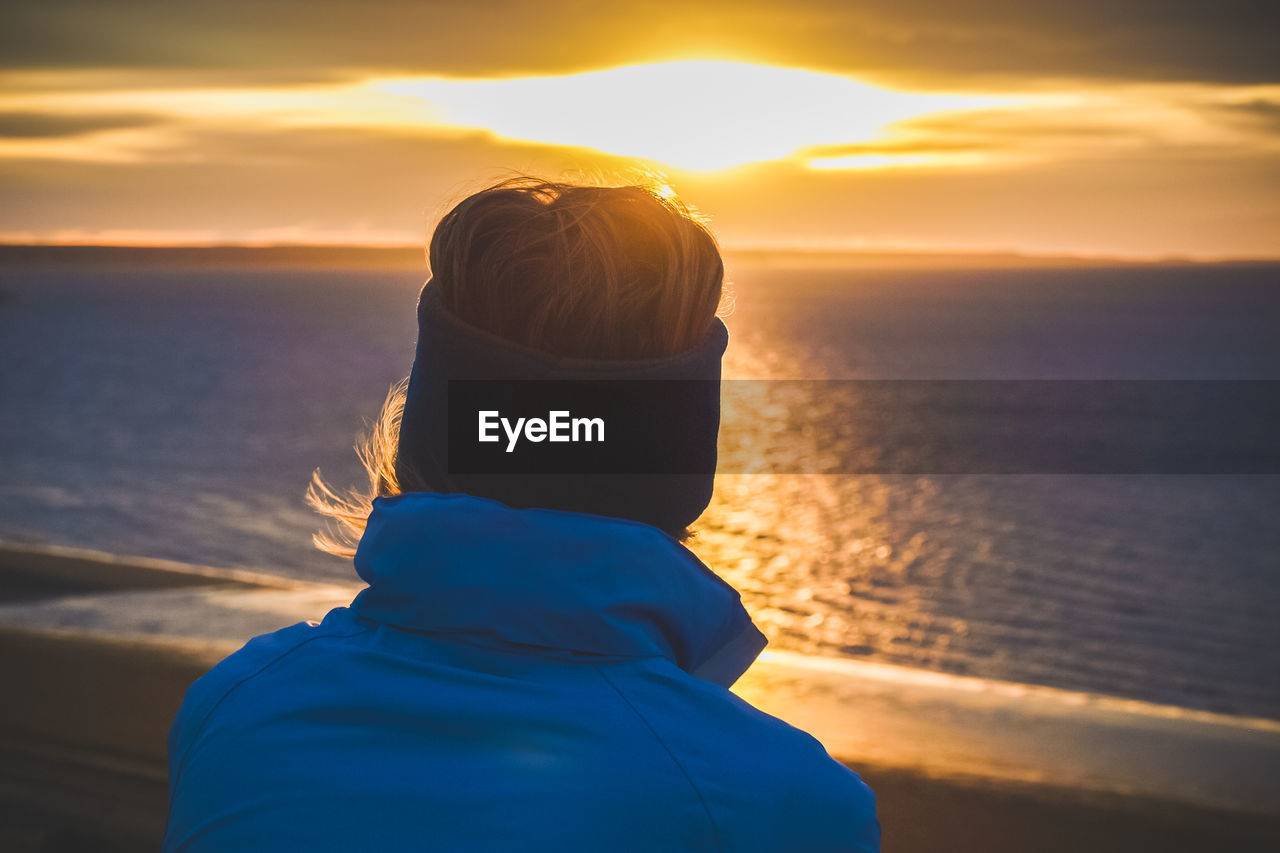 Rear view of woman standing on shore against sky