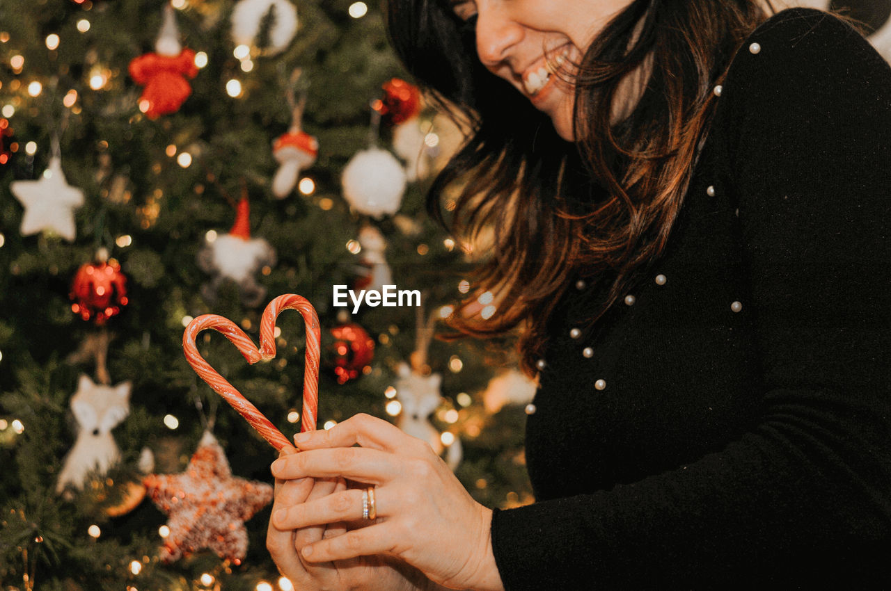 Midsection of woman holding candy cane against christmas tree