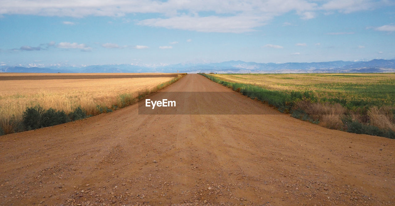 Dirt road amidst field against sky