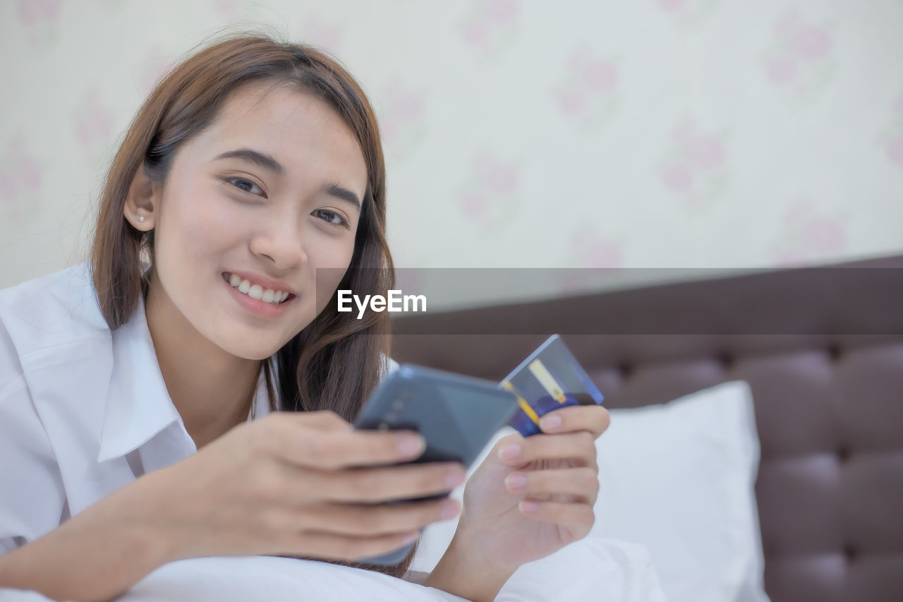 SMILING YOUNG WOMAN USING MOBILE PHONE IN LAPTOP