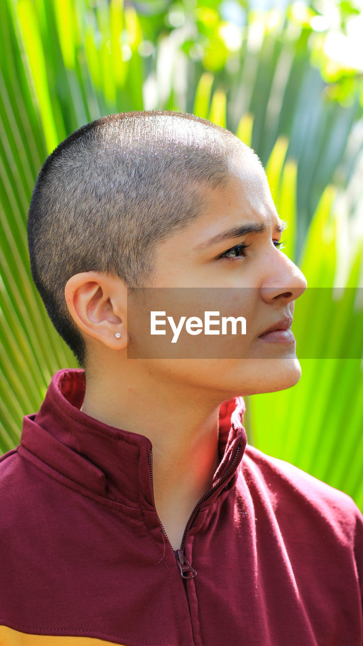 Close-up of woman with shaved head against plants