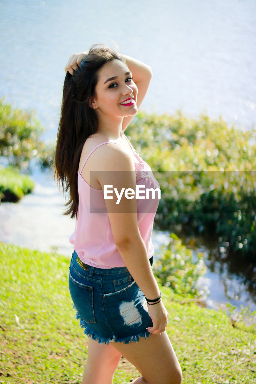 Portrait of smiling young woman standing by lake