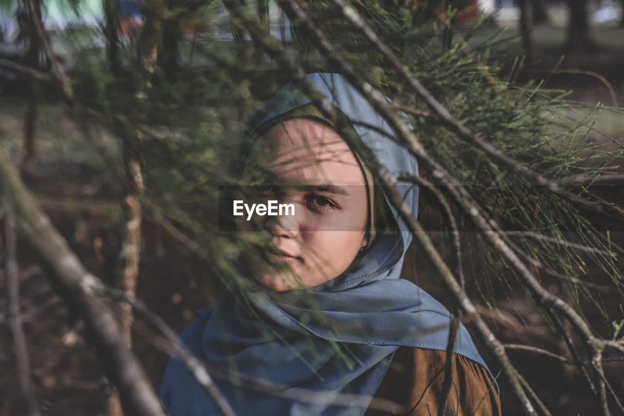 Portrait of young woman seen through branches in forest