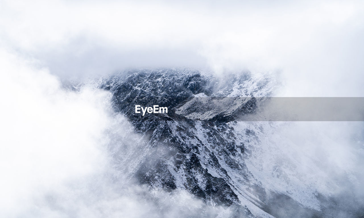 Majestic panoramic scenery of rough rocky slopes of mountain range covered with snow under cloudy sky