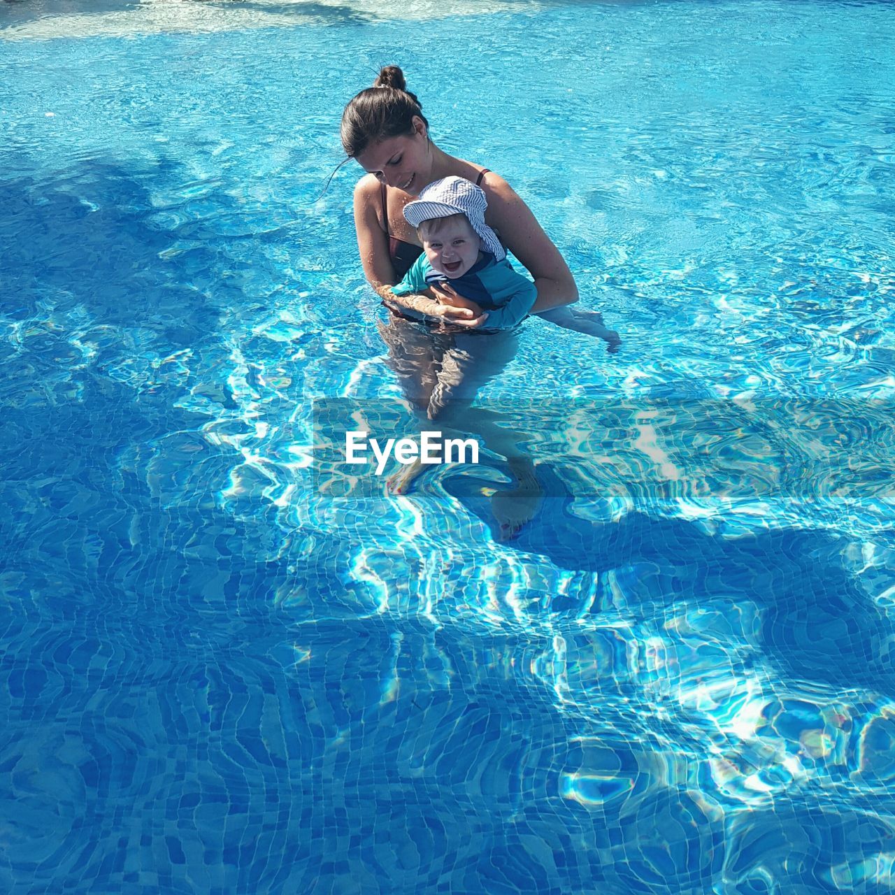 High angle view of happy mother carrying baby in swimming pool