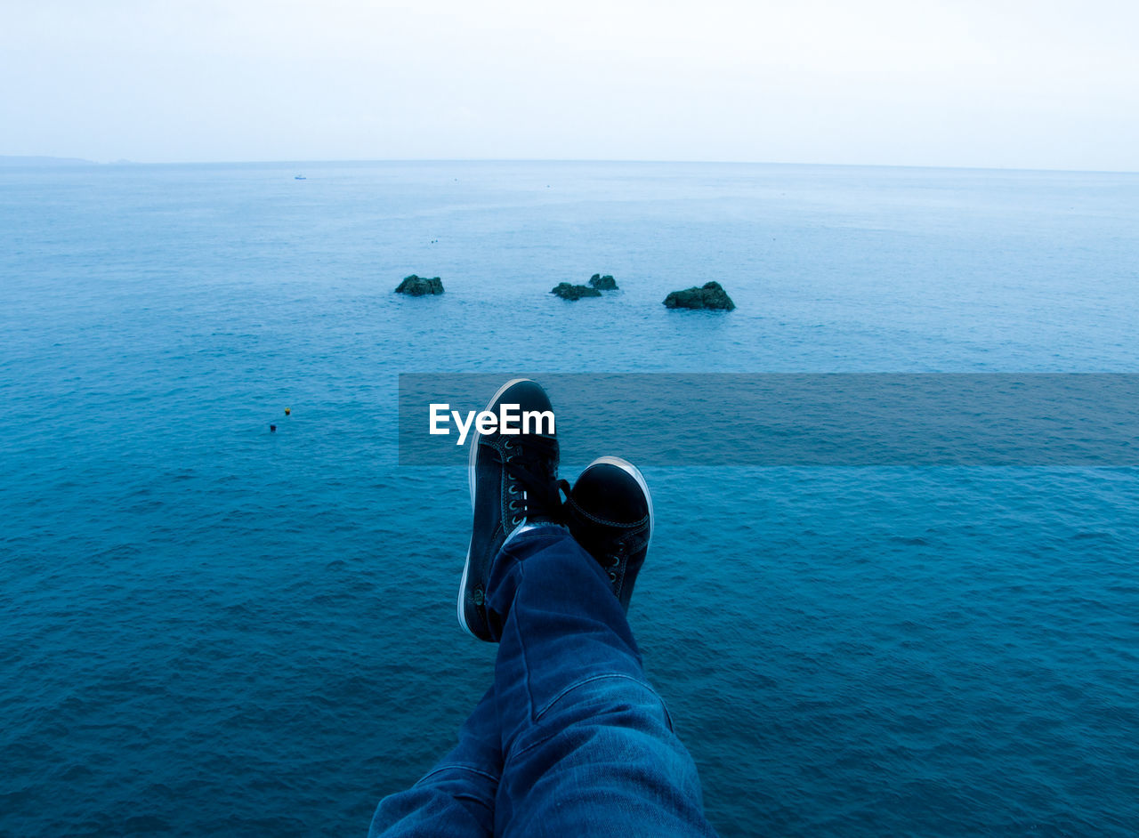 Low section of man sitting over blue sea against sky