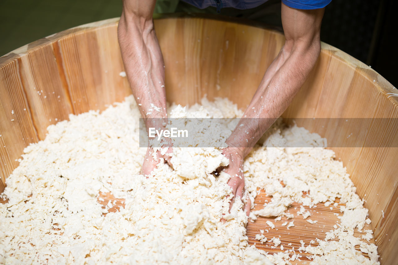 Cropped hands of man crushing cheese in wooden container