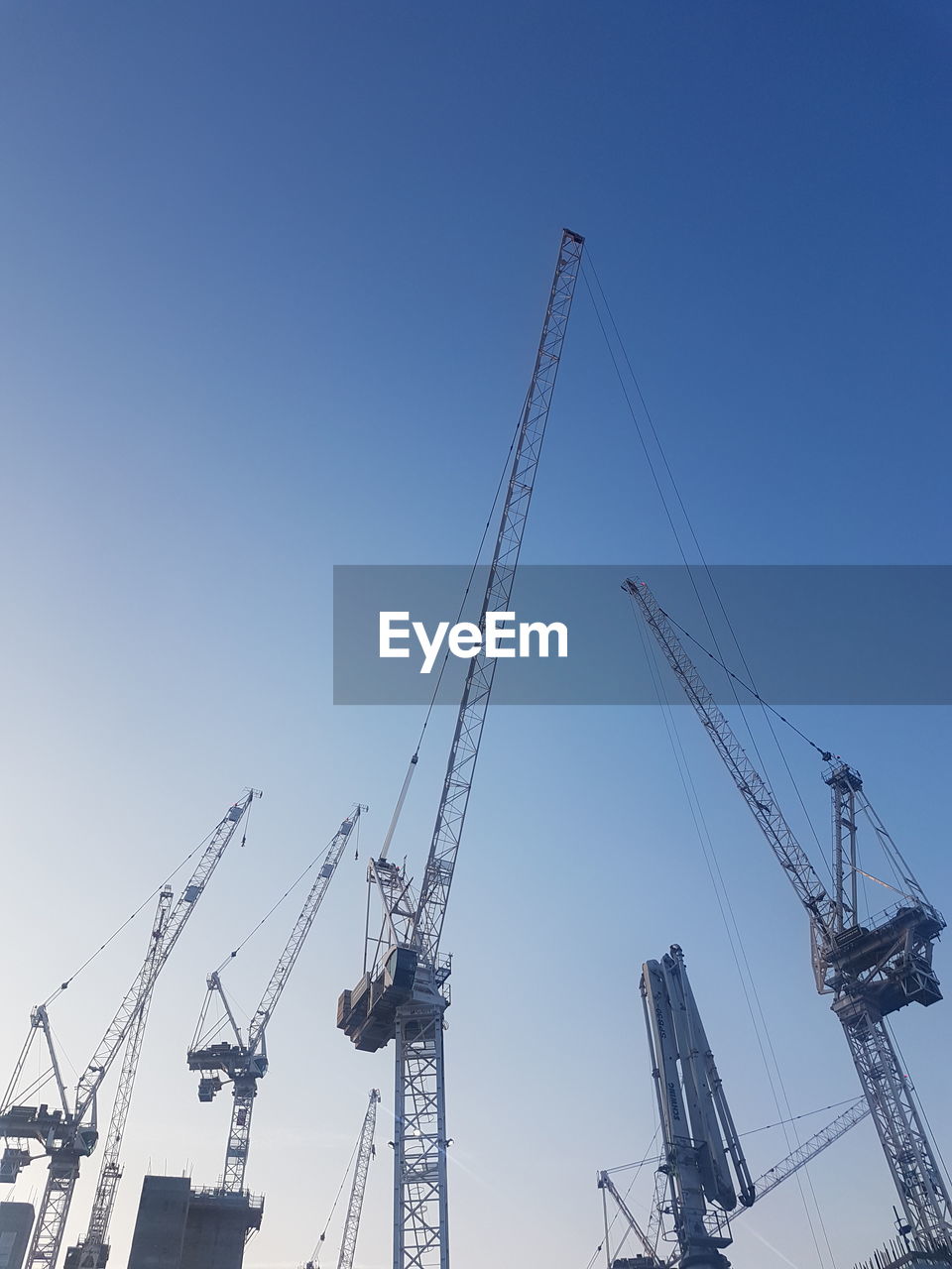 Low angle view of cranes against clear blue sky