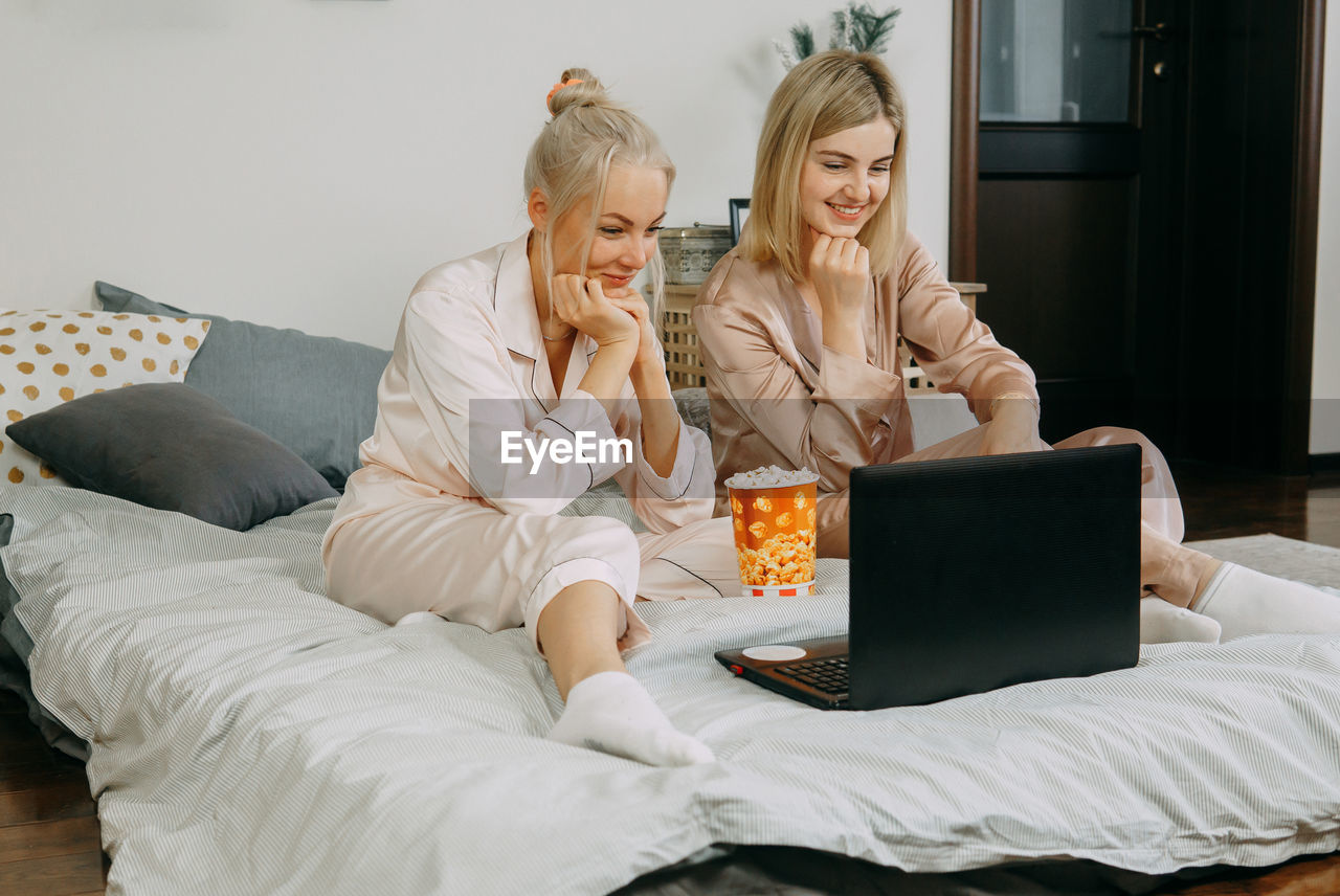 Blonde women at home watching a movie on a laptop and eating popcorn. the concept of friendship. 