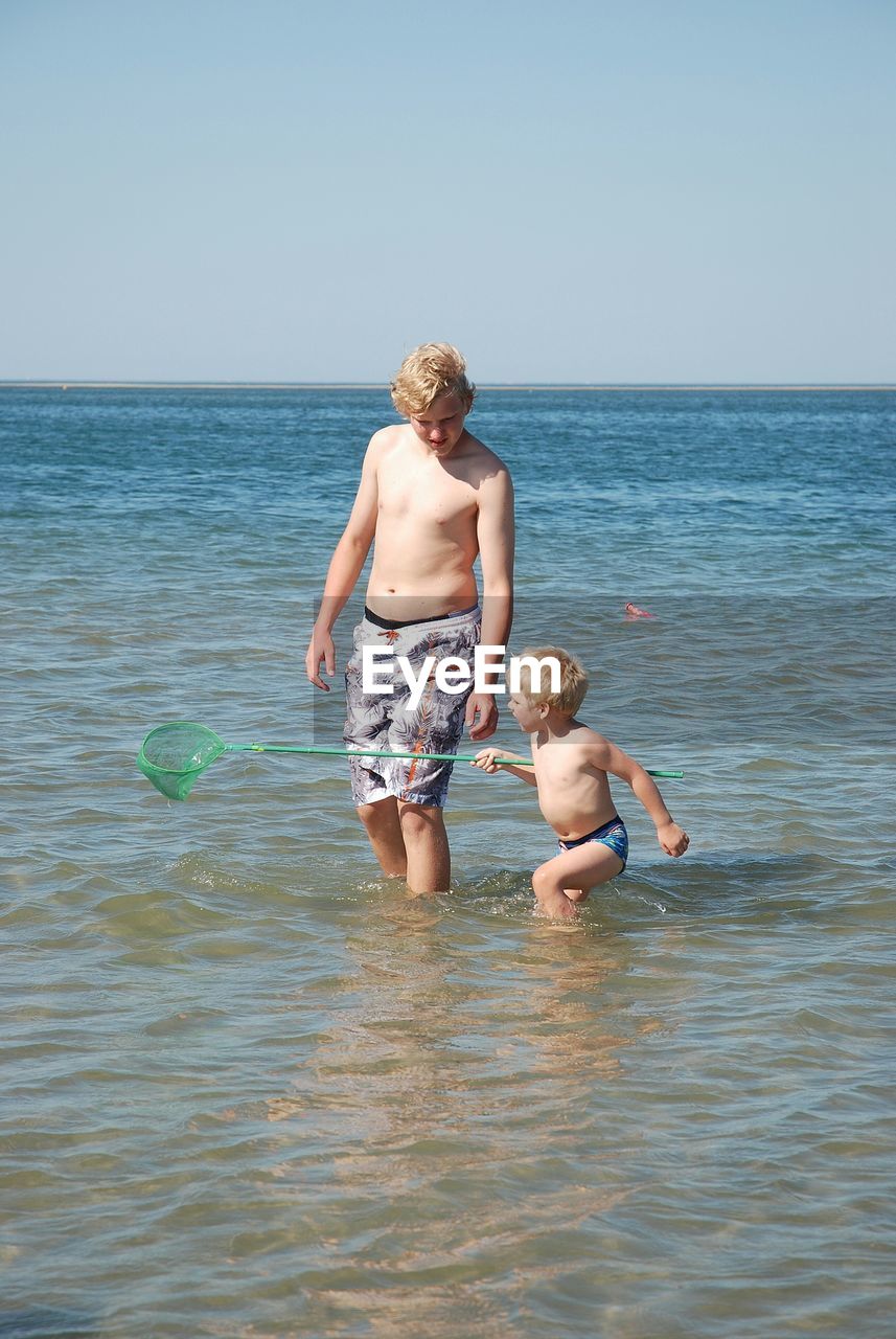 Rear view of shirtless boy in sea against clear sky