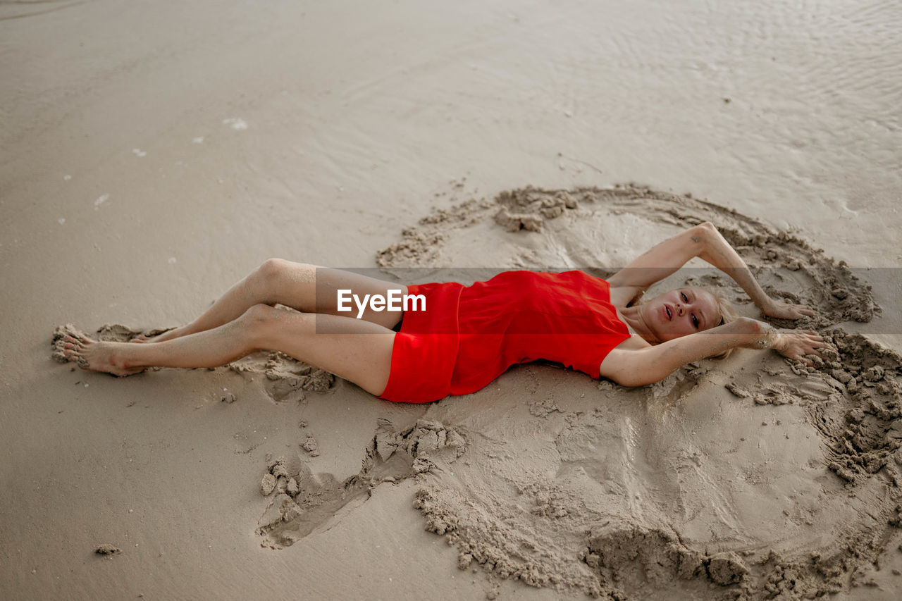 Low section of woman relaxing on sand at beach