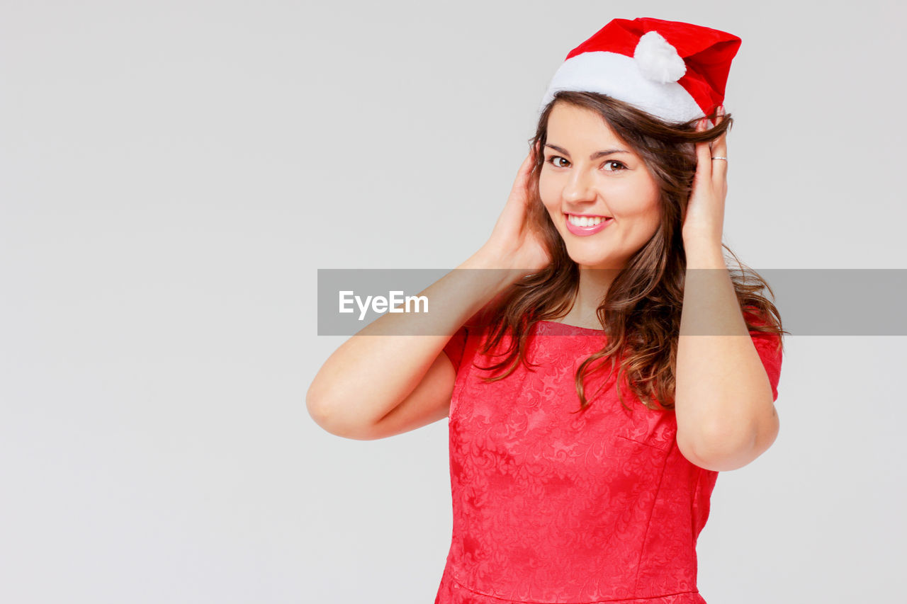 Portrait of happy young woman wearing santa hat while standing against gray background