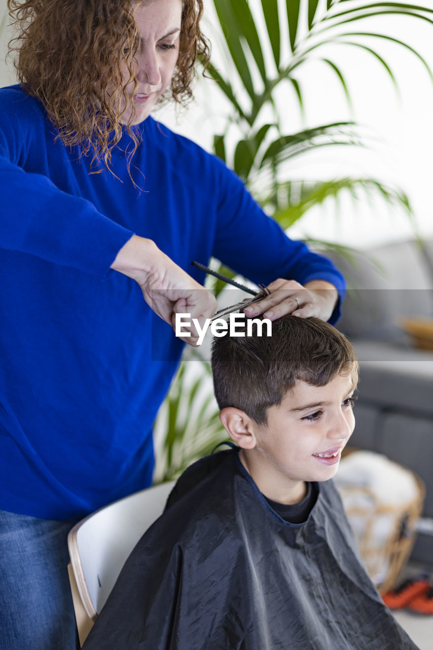 Funny boy getting haircut at home with scissors