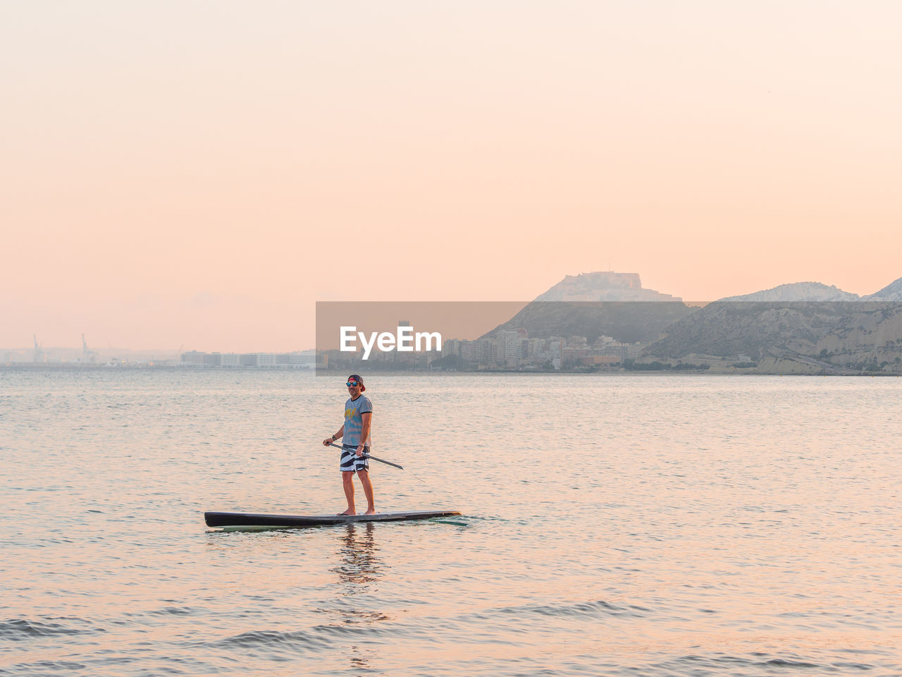 Sporty man swimming on surfboard paddle looking away in alicante spain