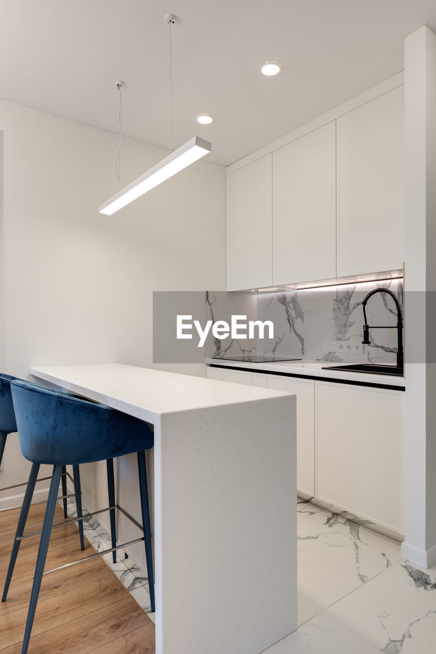 Bright kitchen with white island and blue chairs in a modern style