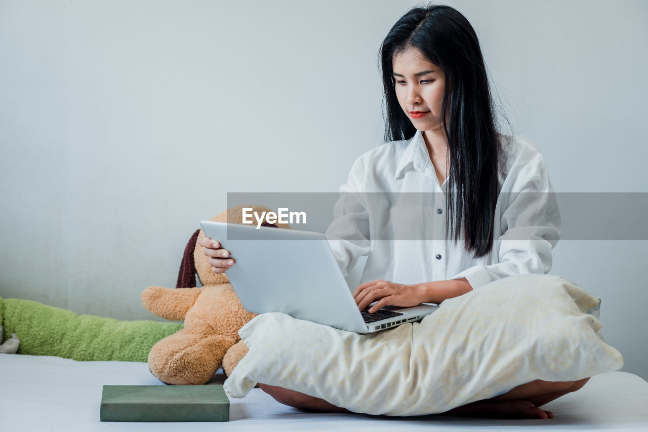 YOUNG WOMAN USING SMART PHONE WHILE SITTING IN LAPTOP