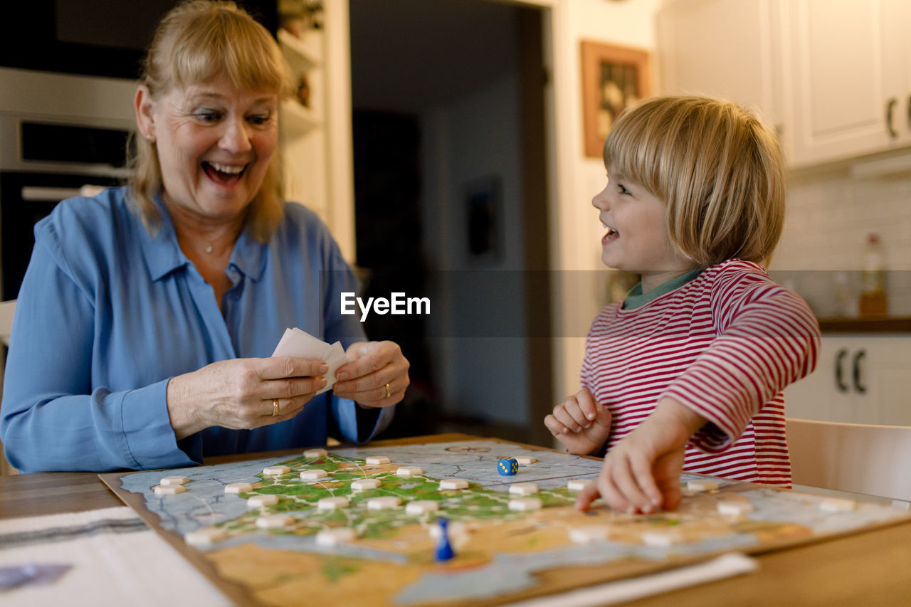 Cheerful grandmother and grandson playing board game at home