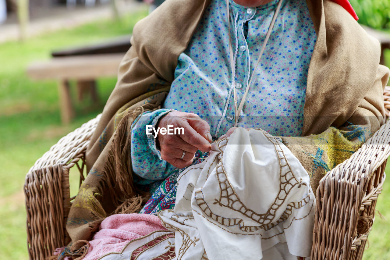  middle section of woman embroidering sitting in basket