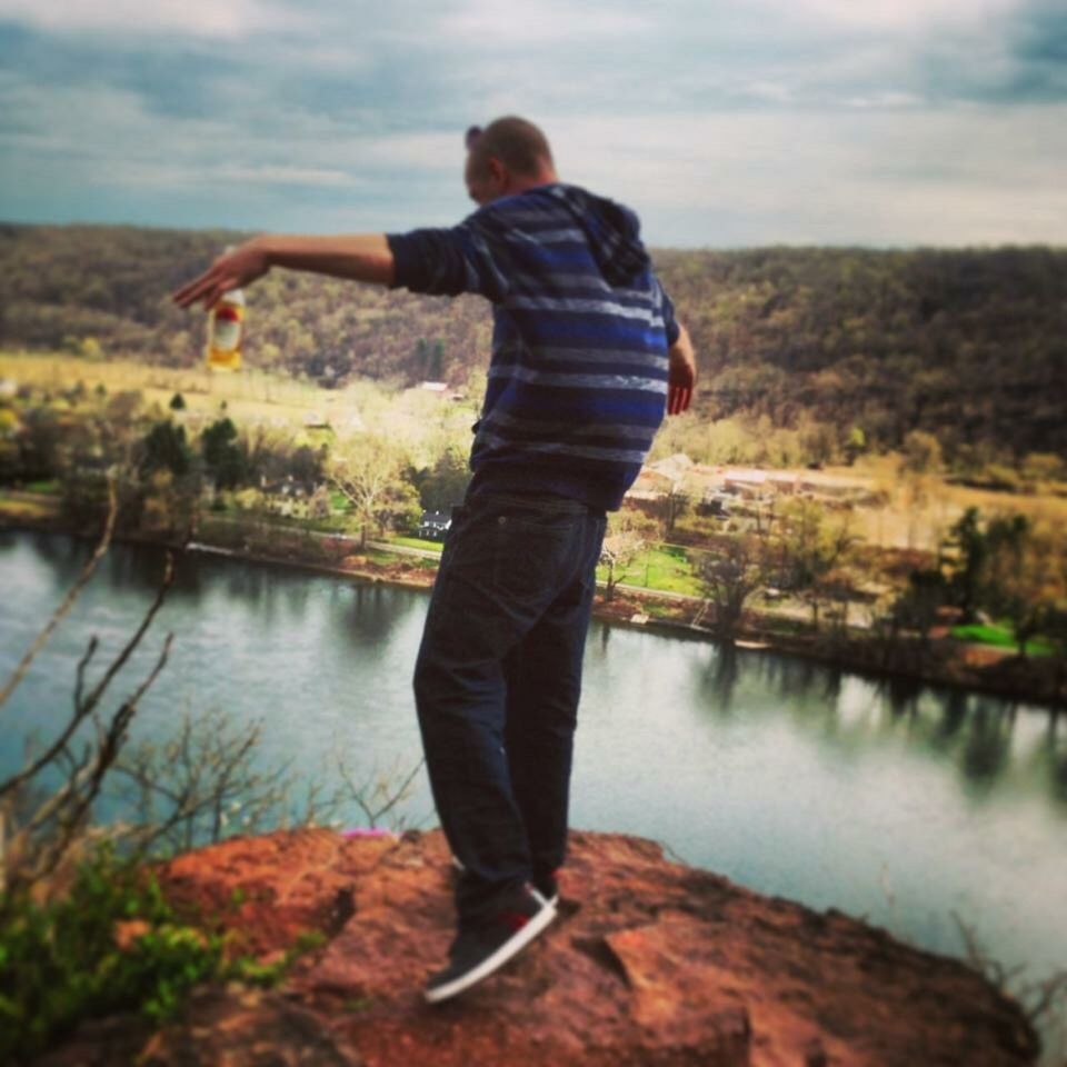 REAR VIEW OF MAN STANDING IN LAKE AGAINST SKY