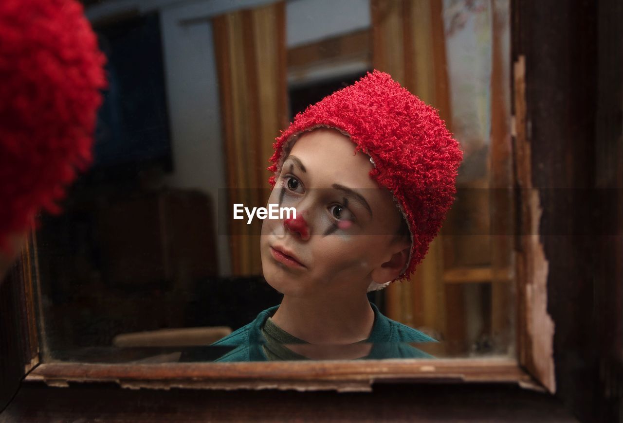 Portrait of boy clown painted face looking at mirror