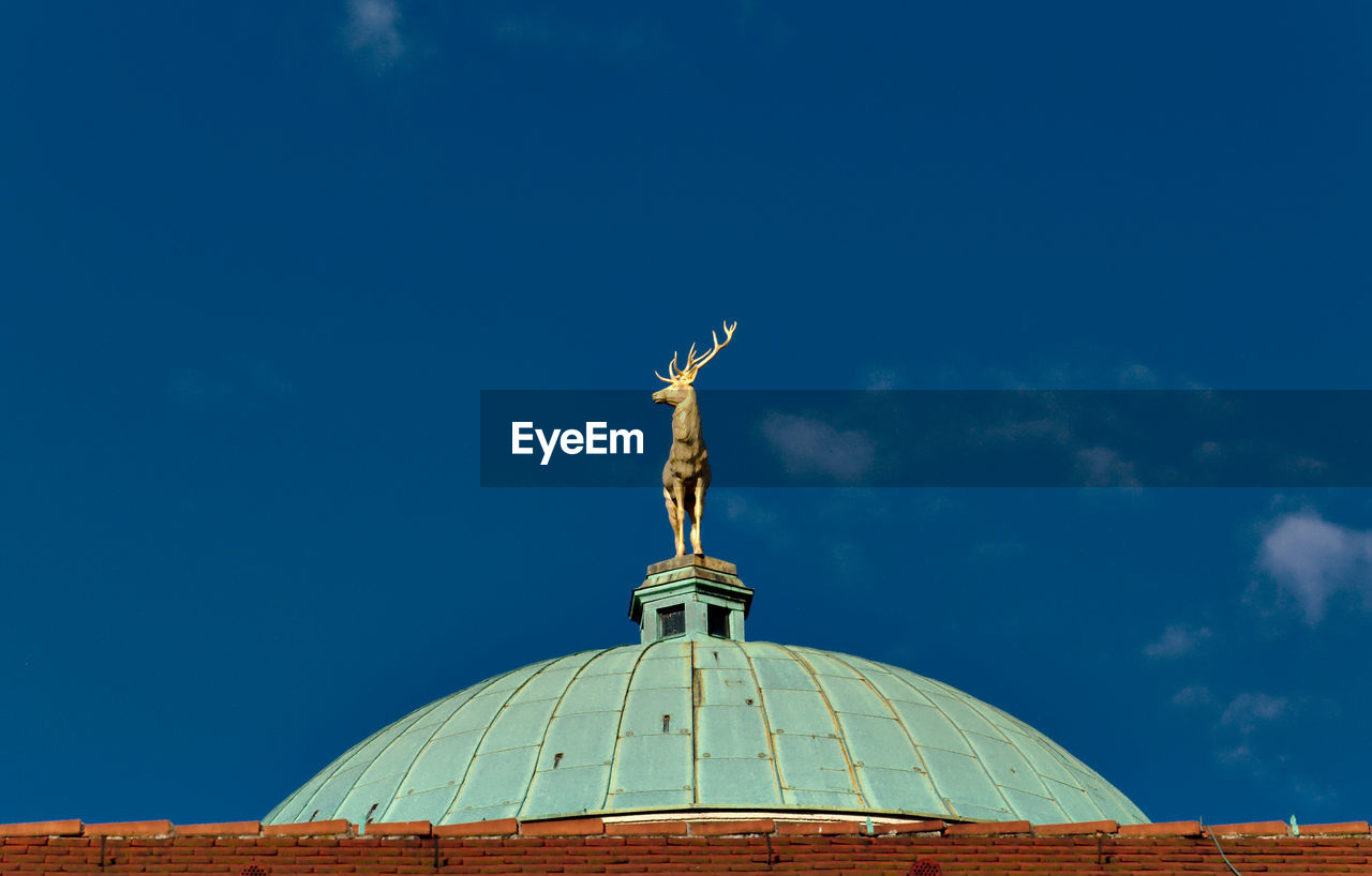 Low angle view of deer statue on dome against blue sky