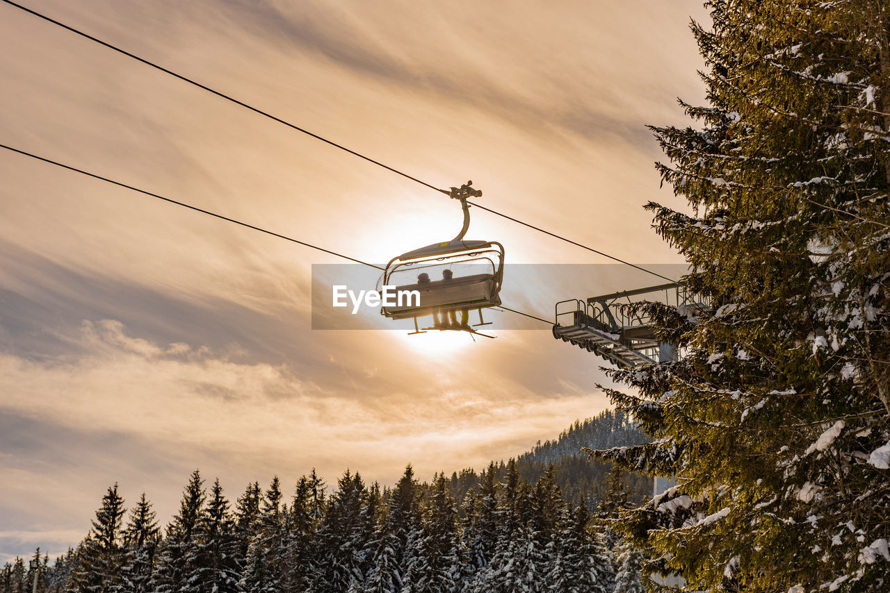 Skiers going up the ski lift, chairlift against the orange sun. snowy mountains, ski slopes, trees