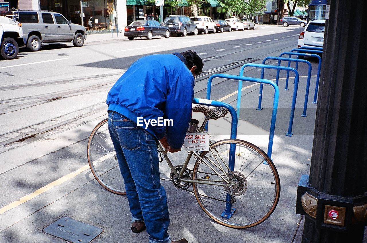 Man locking bicycle on rack at sidewalk