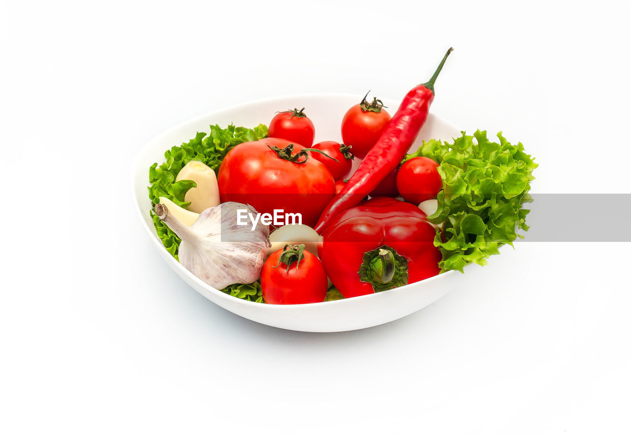 Plate with tomatoes, pepper, garlic, green salad leaves. creative composition isolated on white.
