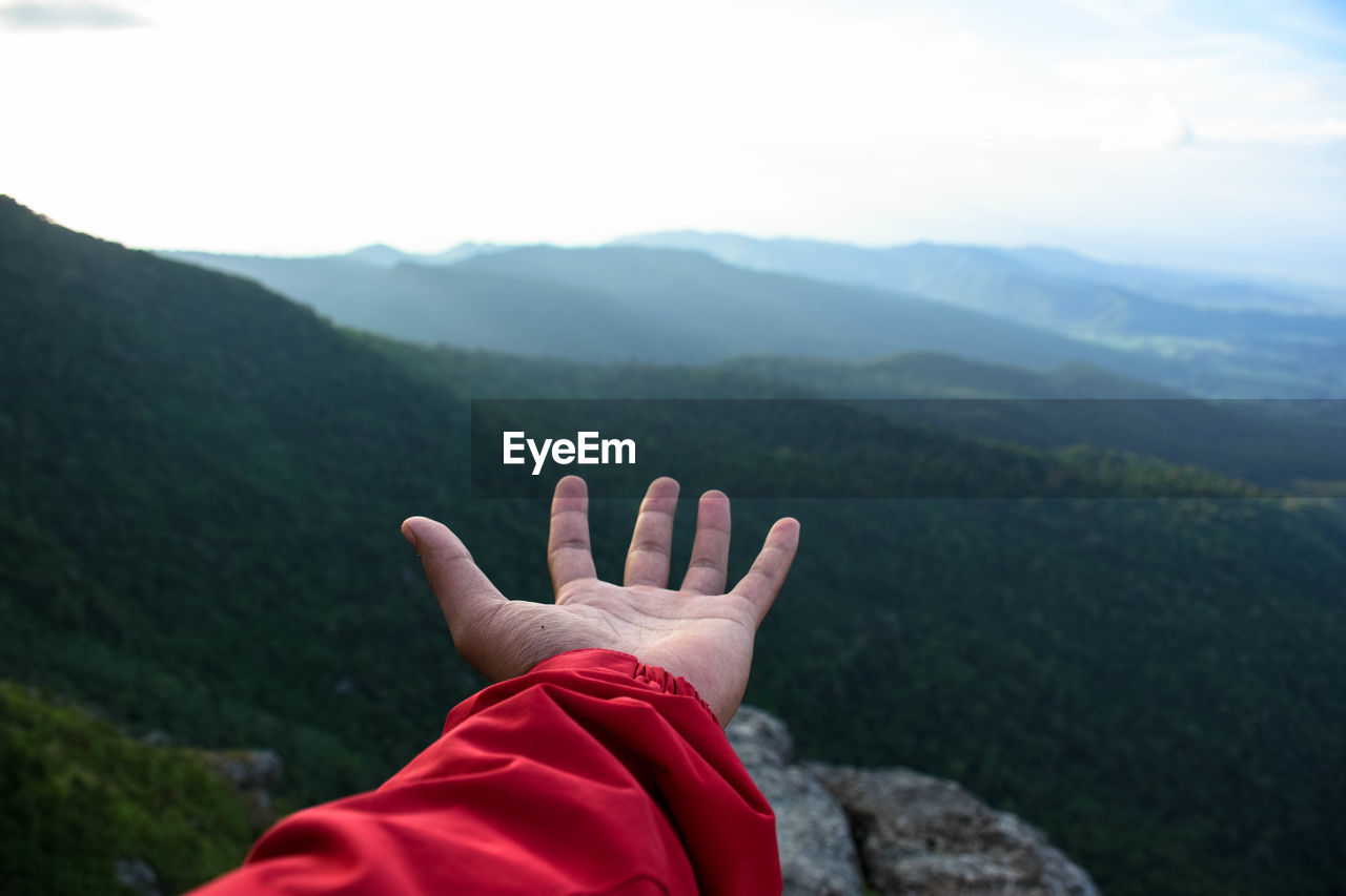 Cropped hand of person by mountain against sky