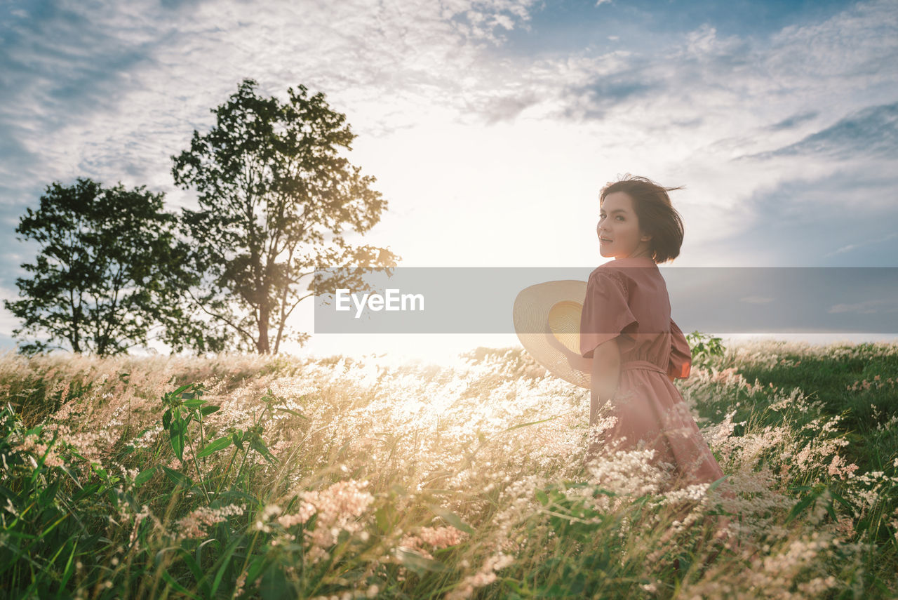 An asian girl on a beautiful spring meadow at sunset. she wears a pink dress and wide-brimmed hat.