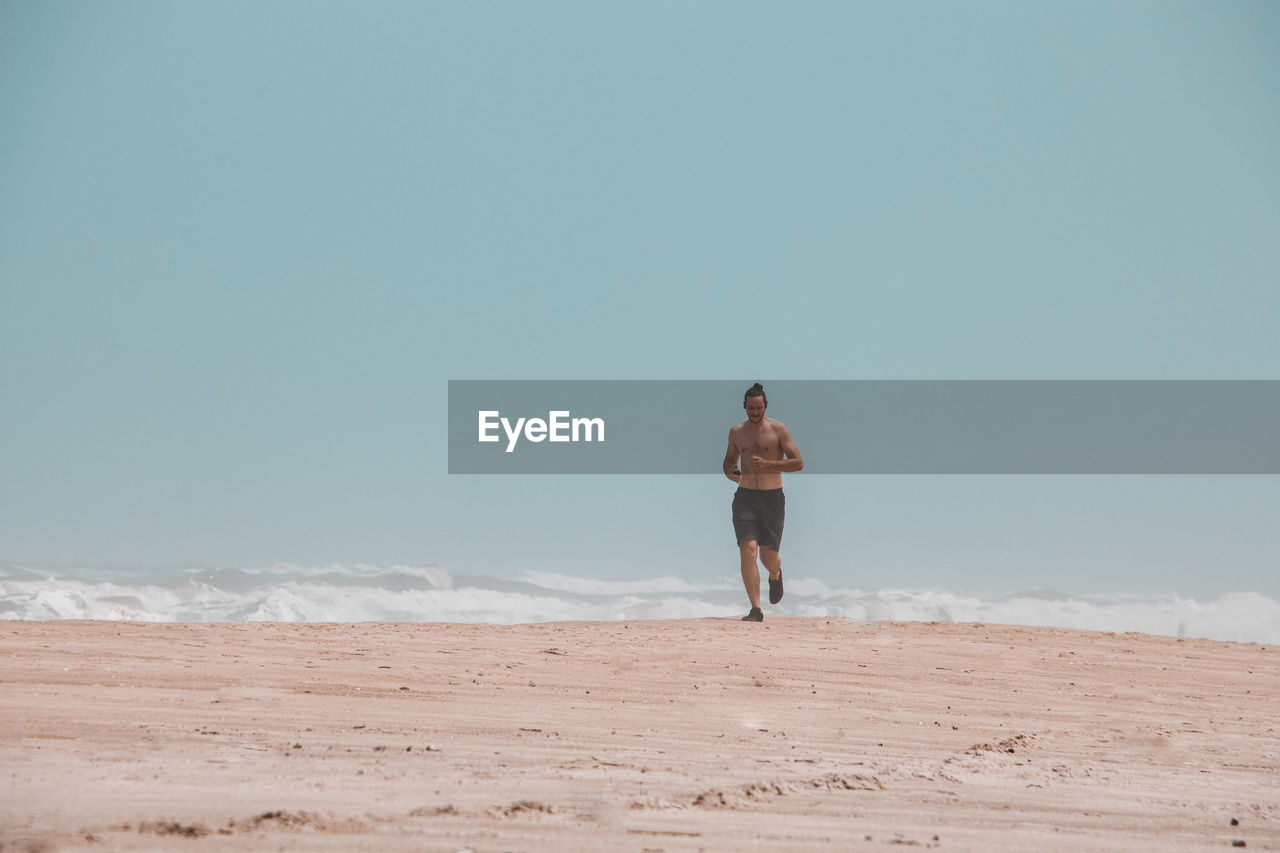 Shirtless man running at beach against sky