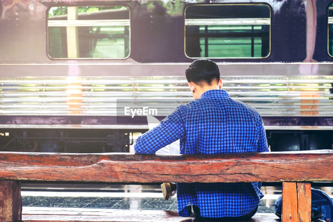 Rear view of man sitting at railroad station platform