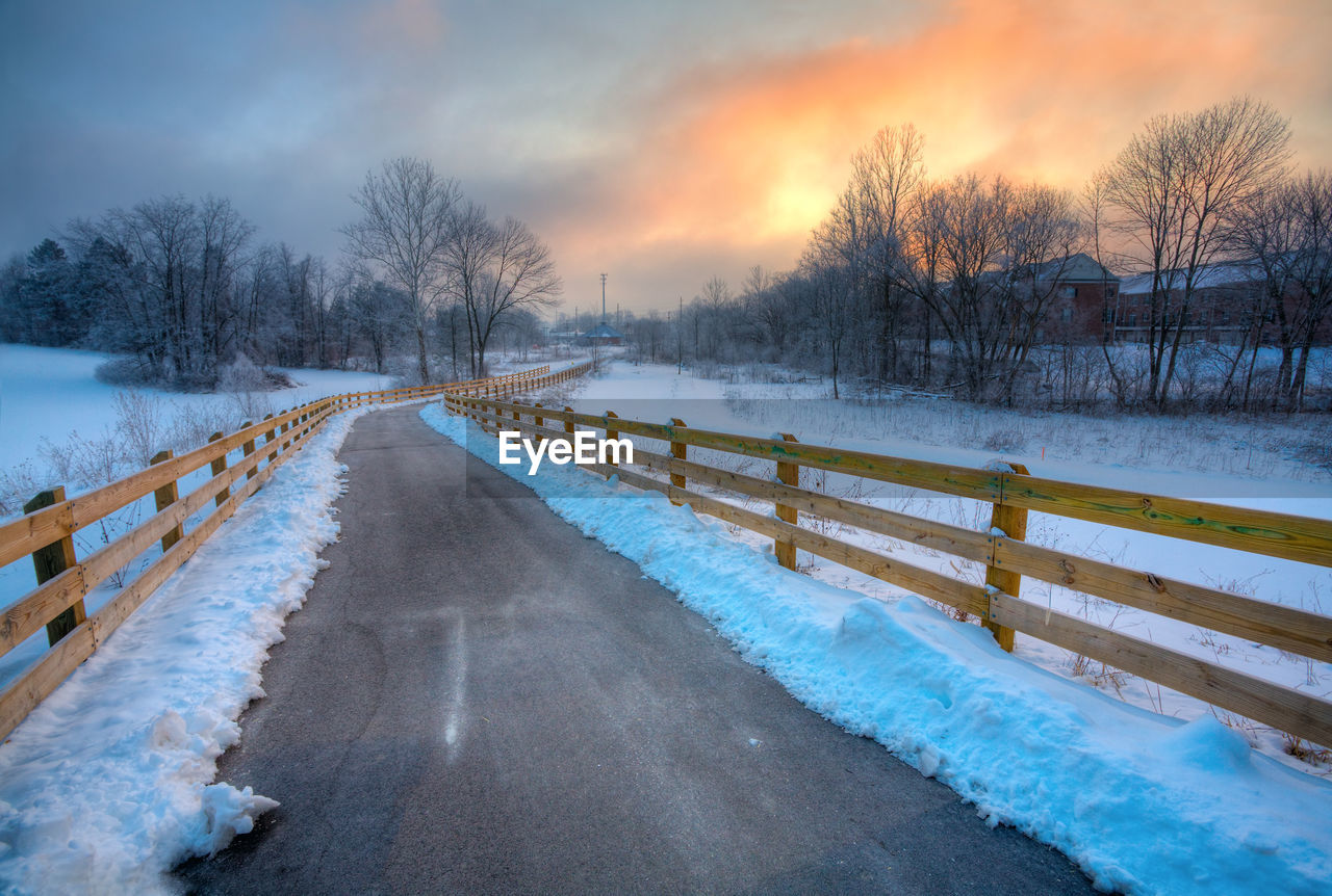 SNOW COVERED ROAD BY BARE TREES AGAINST SKY